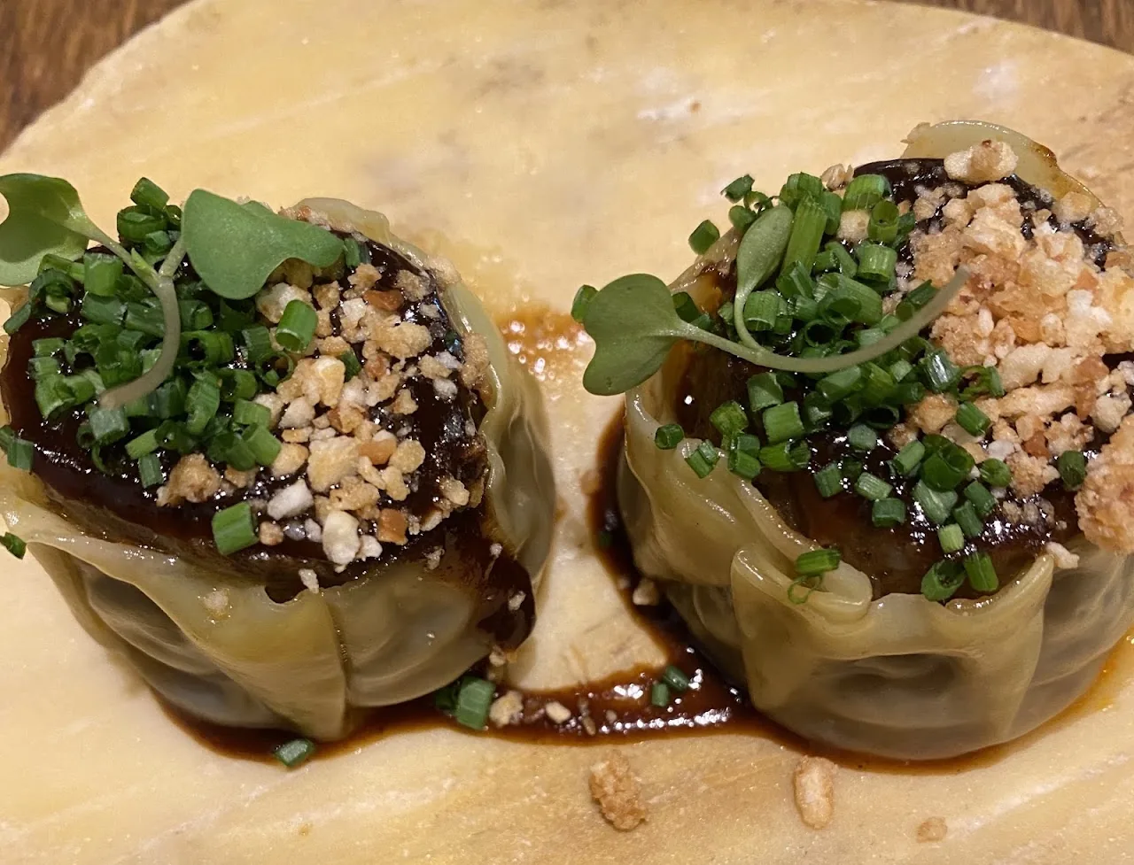 Two wrapped dumplings garnished with herbs and crushed nuts in sauce