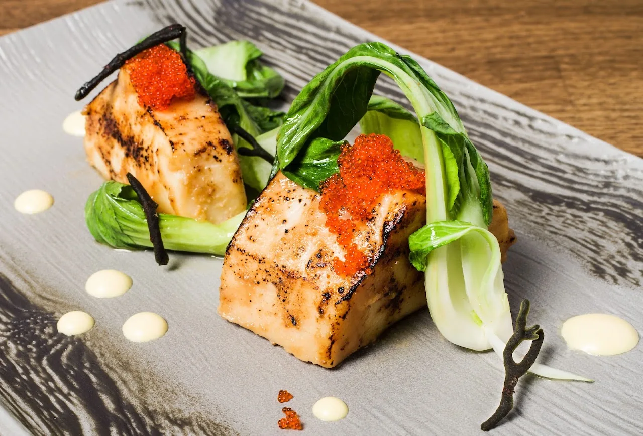 A grilled fish fillet with bok choy and red sauce on a plate