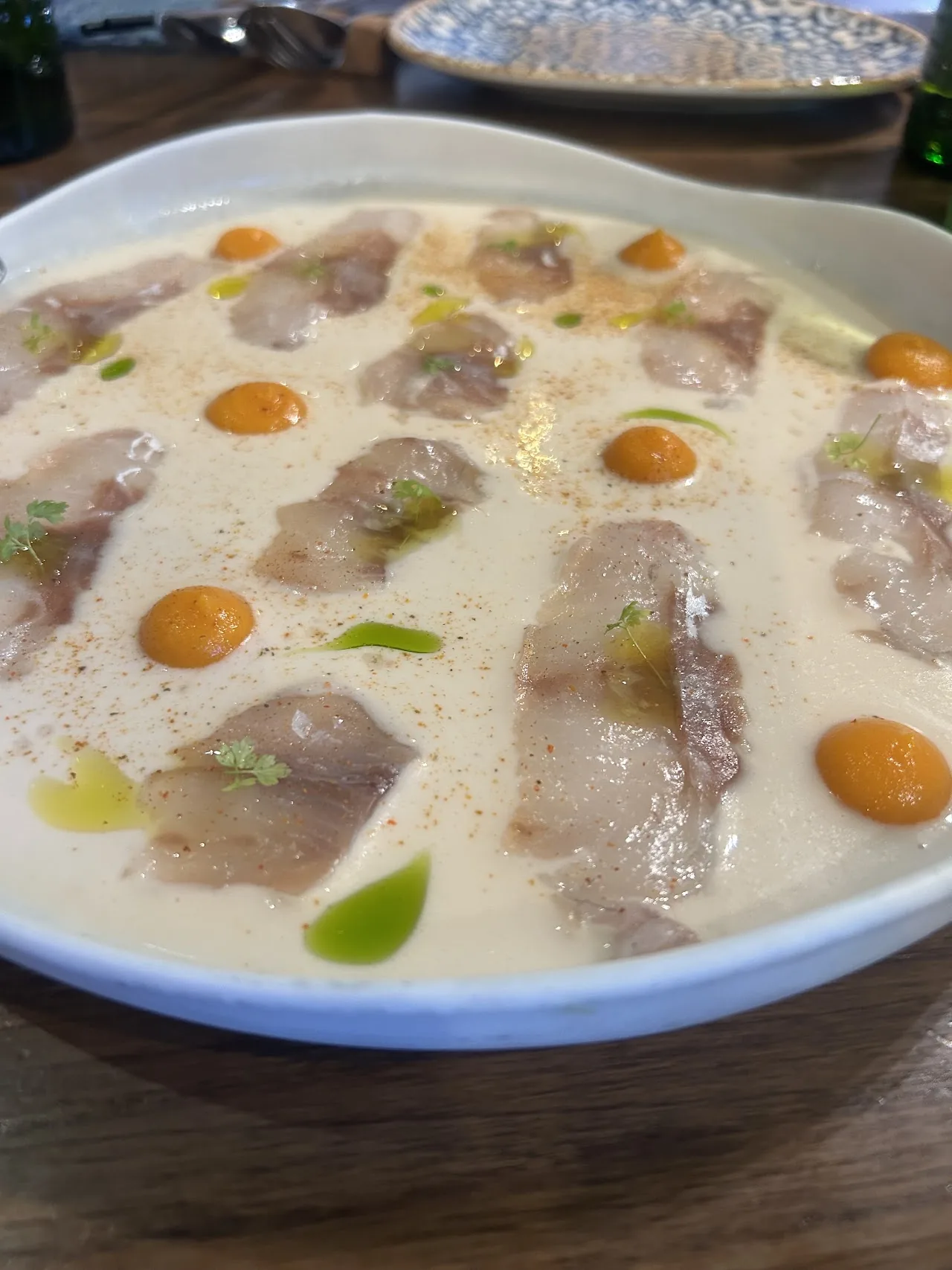 Thinly sliced fish in a creamy broth with orange dots of sauce