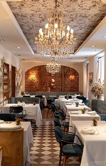 Dining room with crystal chandeliers, exposed brick arch, checkerboard tile floor and white-linen tables