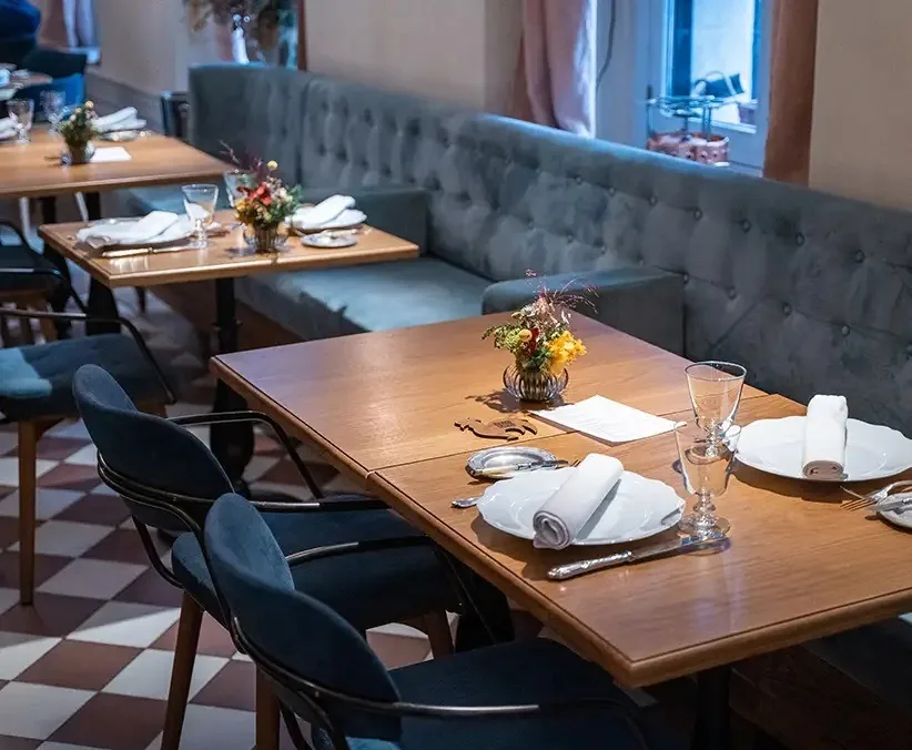 Wooden tables with place settings beside a blue-grey banquette and a checkerboard floor