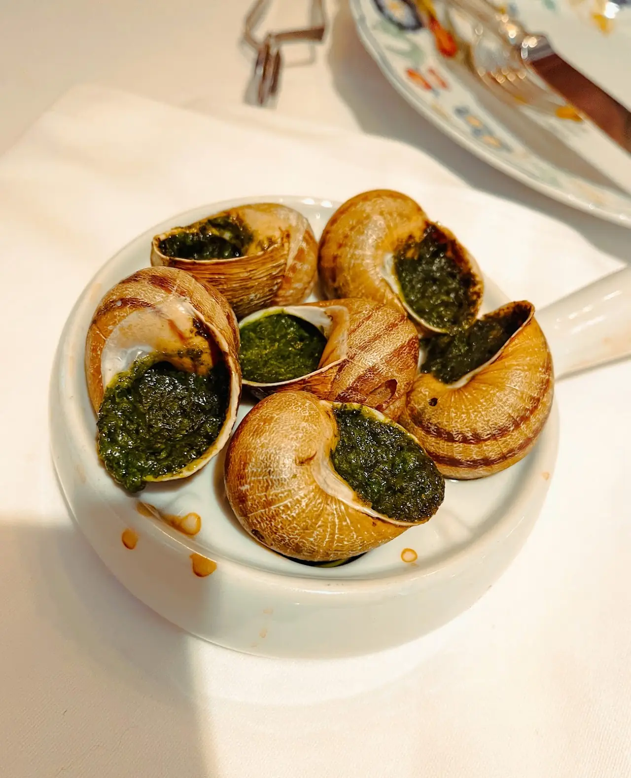Escargots in their shells topped with green herb butter on a white plate.