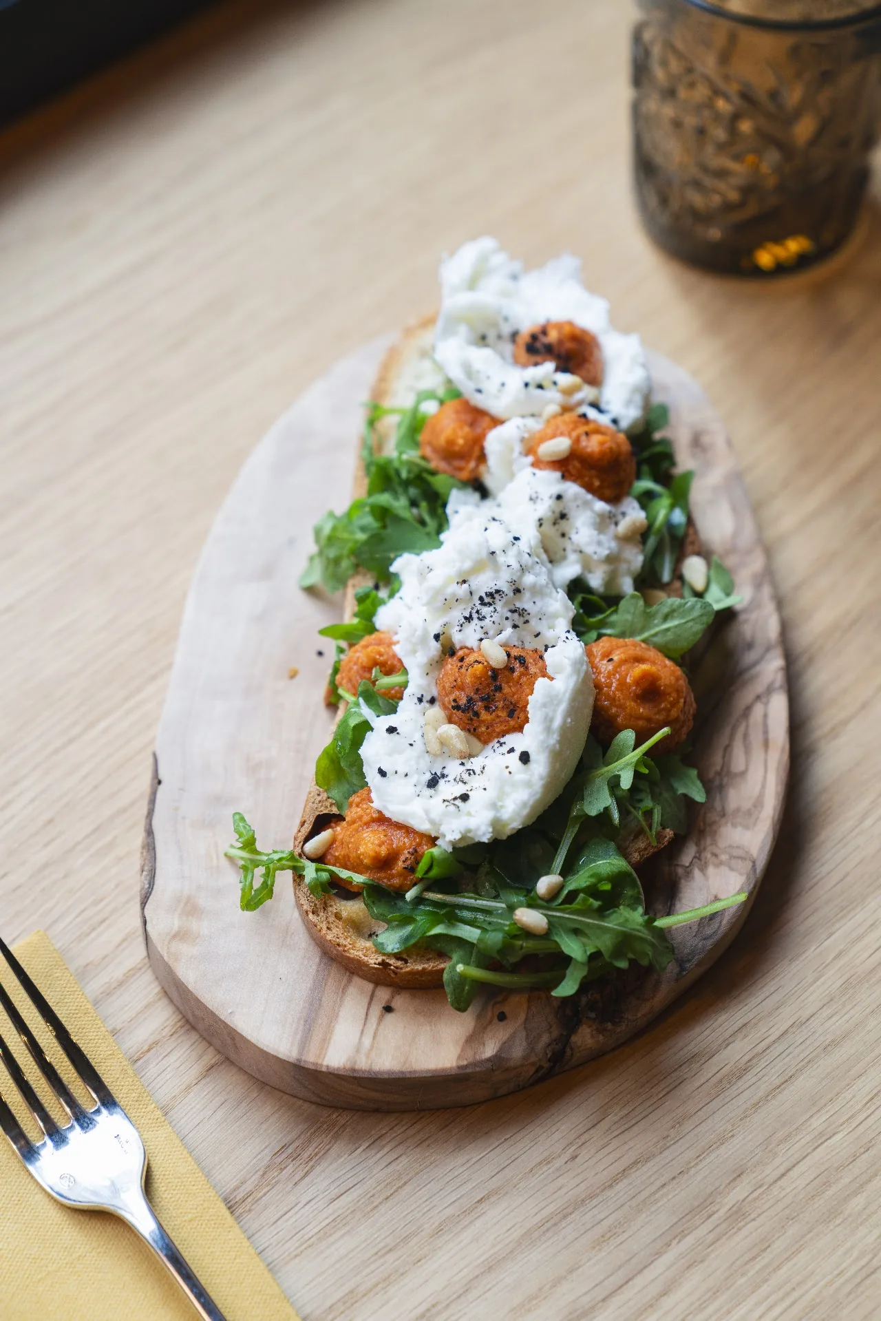 Burrata with roasted tomatoes and greens on a wooden board