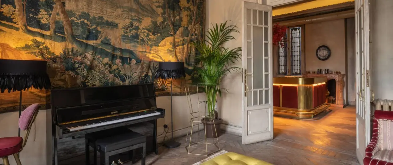 Wide view of the same tapestry-walled piano lounge opening into a bar area with a curved brass and red-velvet counter
