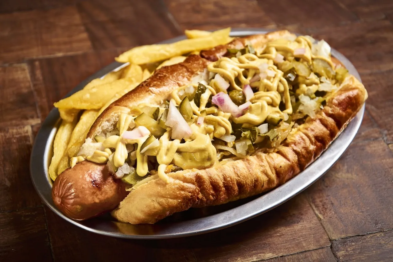 A large grilled sausage in a bun topped with sauerkraut and fries
