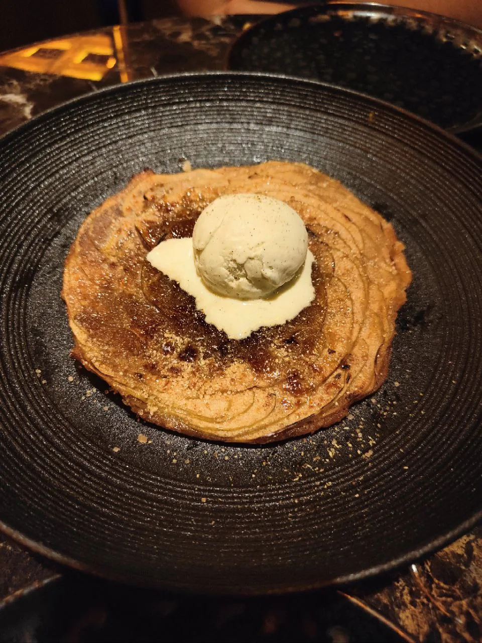 A dark pancake dessert topped with a scoop of ice cream