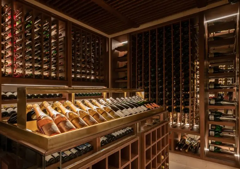 Wood-panelled wine cellar with racks of bottles and an illuminated brass display of rose Champagne