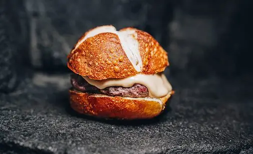 Cheeseburger with melted cheese on a golden toasted bun against a dark stone background