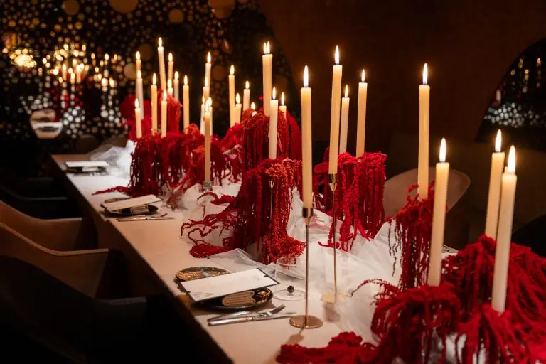Candlelit dining table with tall white tapers and cascading red dried flowers over a white runner