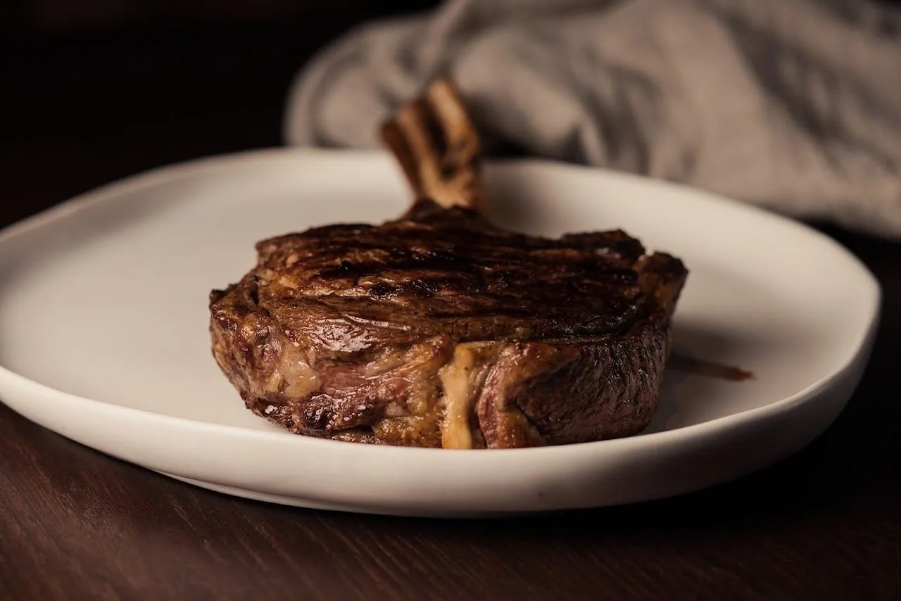 A seared steak on a white plate against a dark background