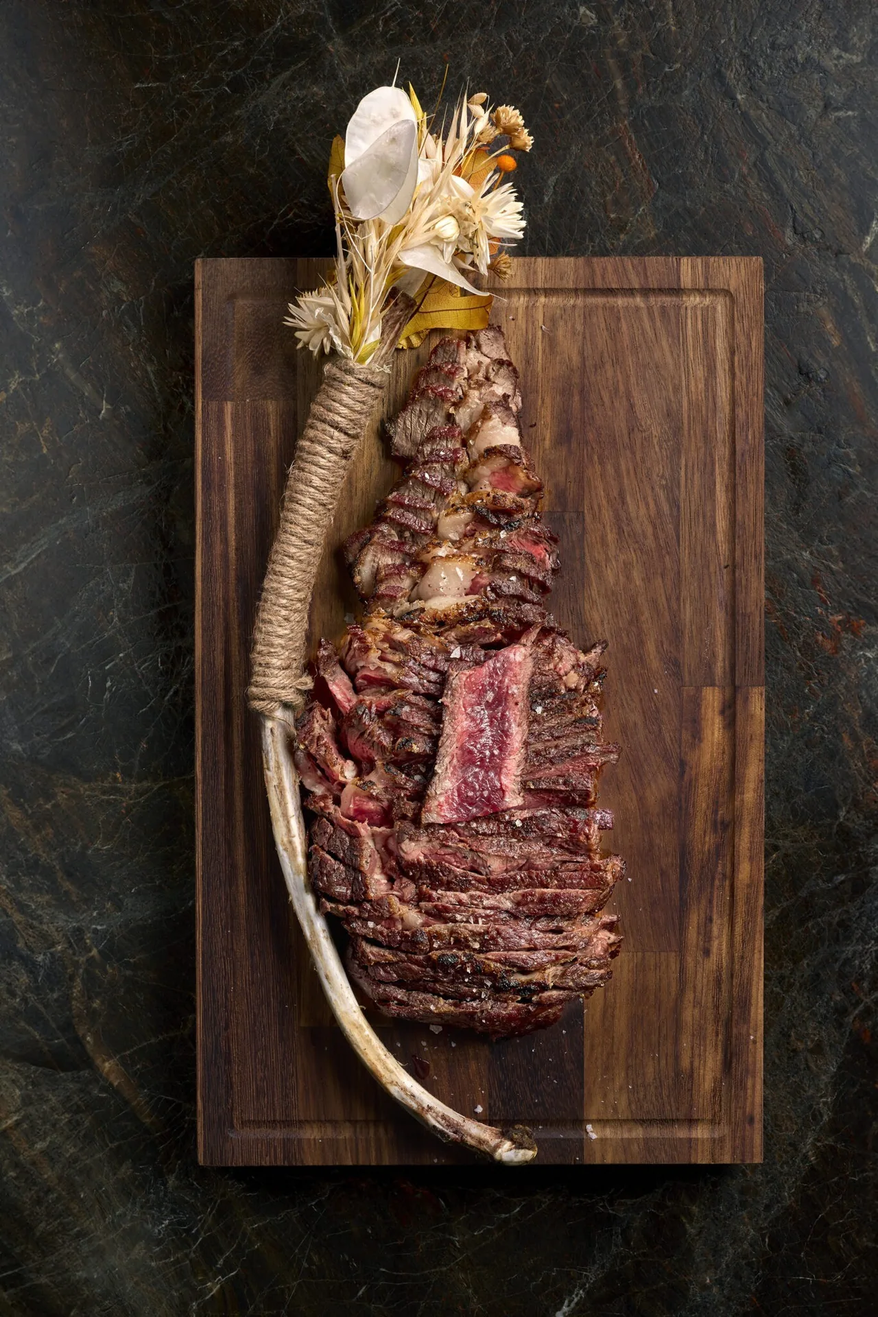 A grilled bone-in steak on a wooden board with a dried decorative stem