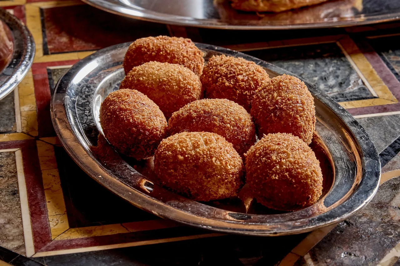 Round golden croquetas on an ornate silver oval tray on a patterned marble table