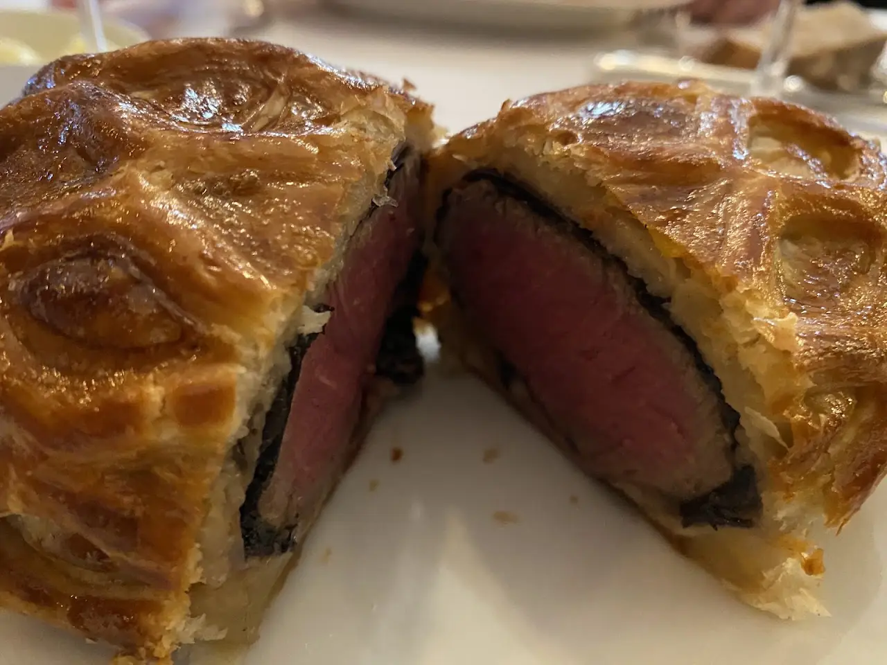 A beef Wellington cut in half, showing pink meat wrapped in golden pastry and mushroom duxelles.