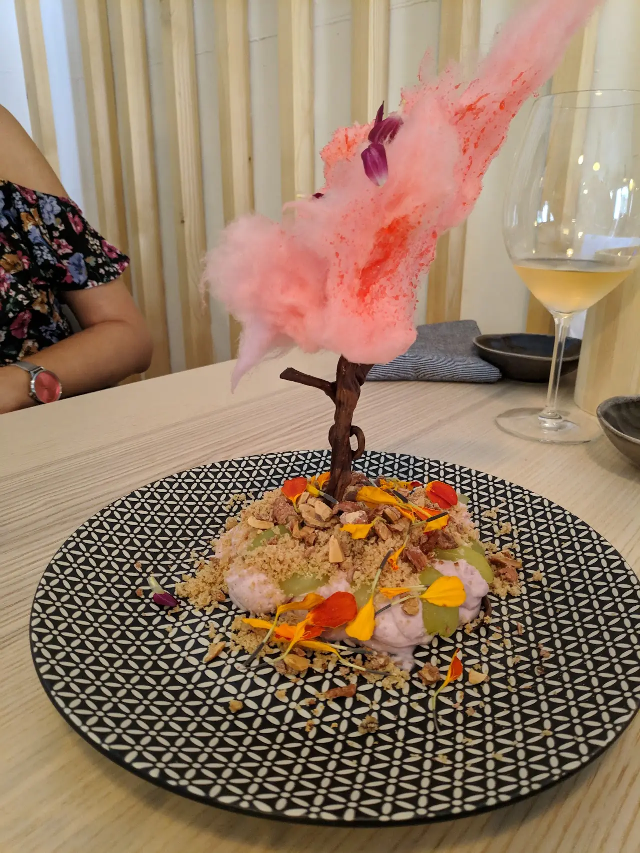 Creative plated course topped with pink cotton candy on a branch, with colorful garnishes on a patterned plate, at L'Home dels Nassos.