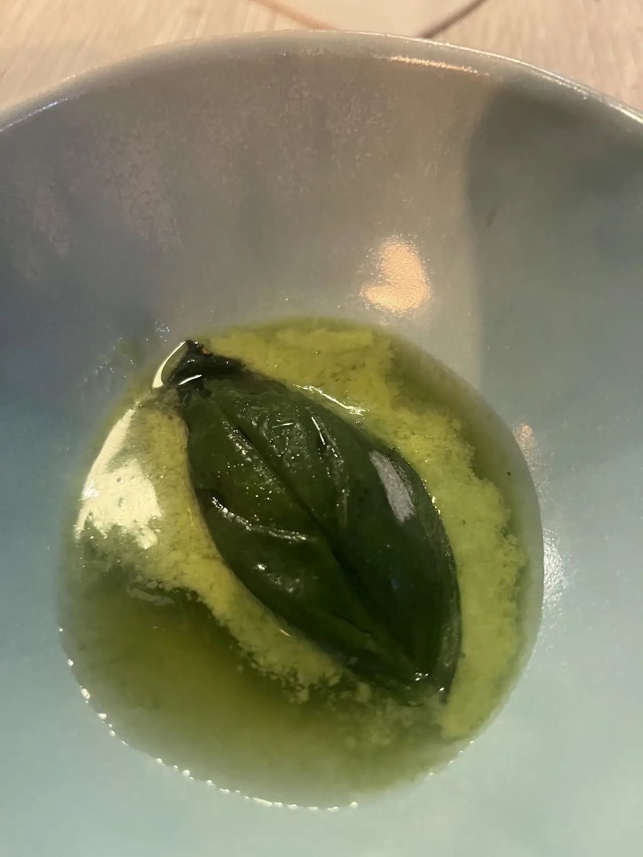 Green herb-oil soup with a single leaf floating on top in a white bowl, at L'Home dels Nassos.