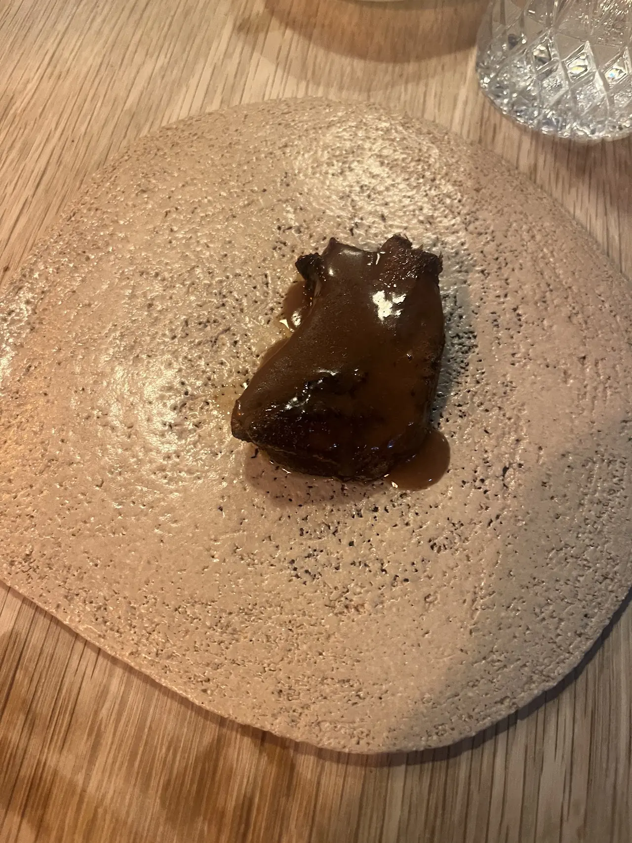 Dark glazed piece of slow-cooked meat on a speckled ceramic plate, at L'Home dels Nassos.