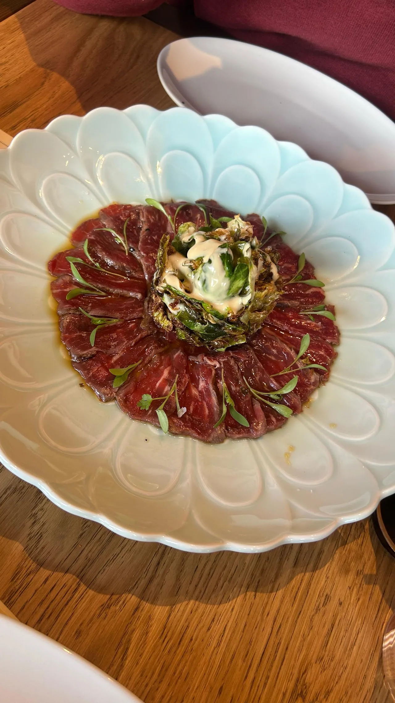 A round plate of thinly sliced beef carpaccio with garnish