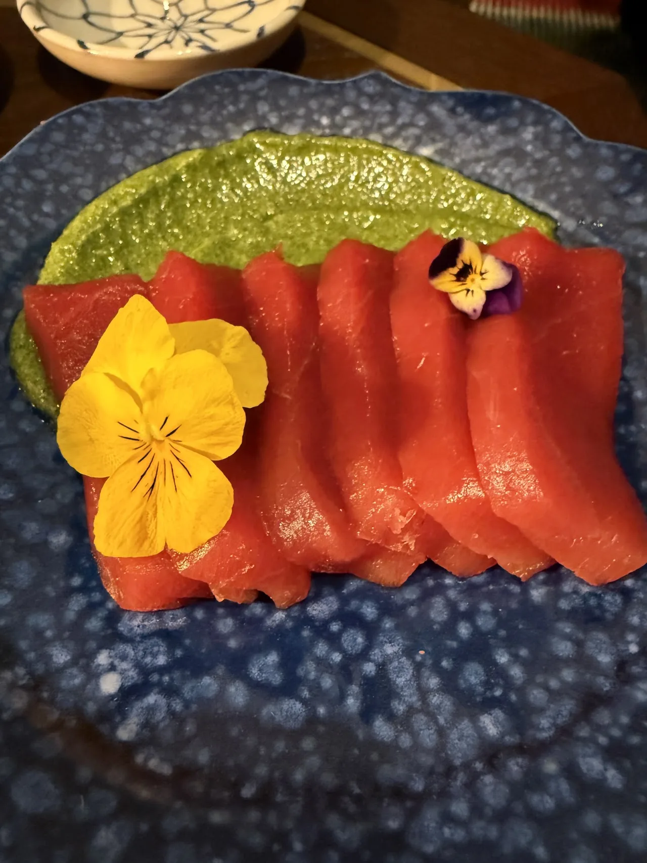 Sliced salmon sashimi fanned on a plate with edible flowers