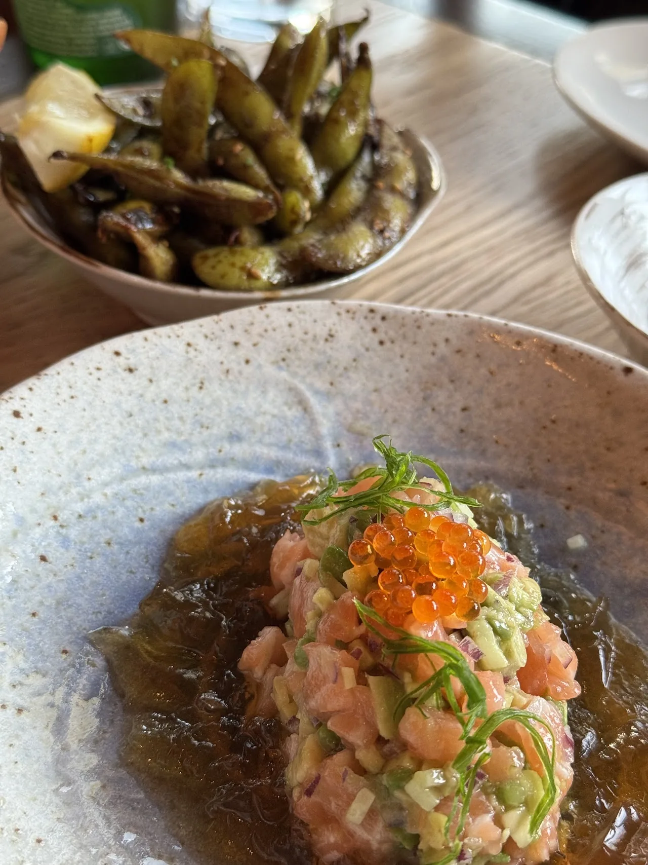 A tartare dish topped with salmon roe over a green sauce, edamame beside