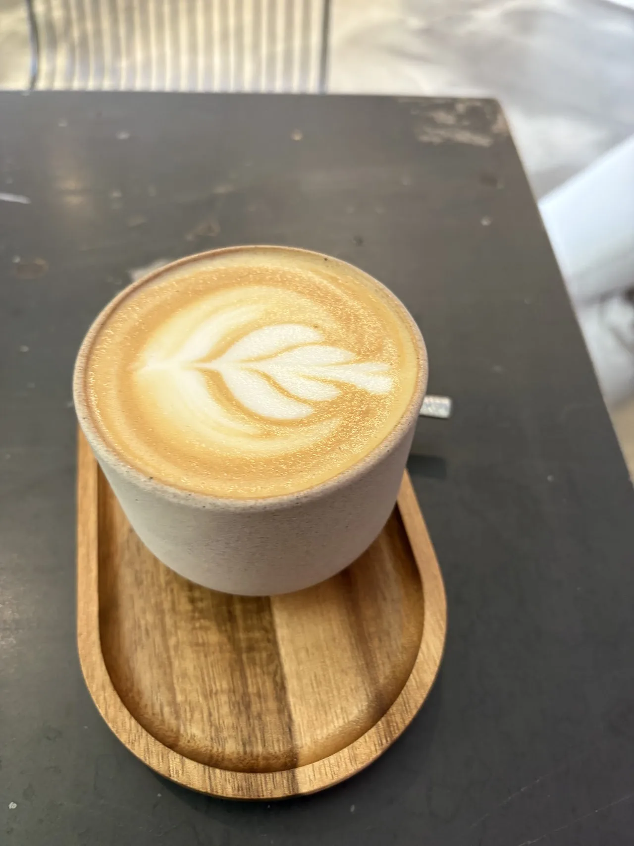 A latte with leaf-pattern latte art on a wooden tray