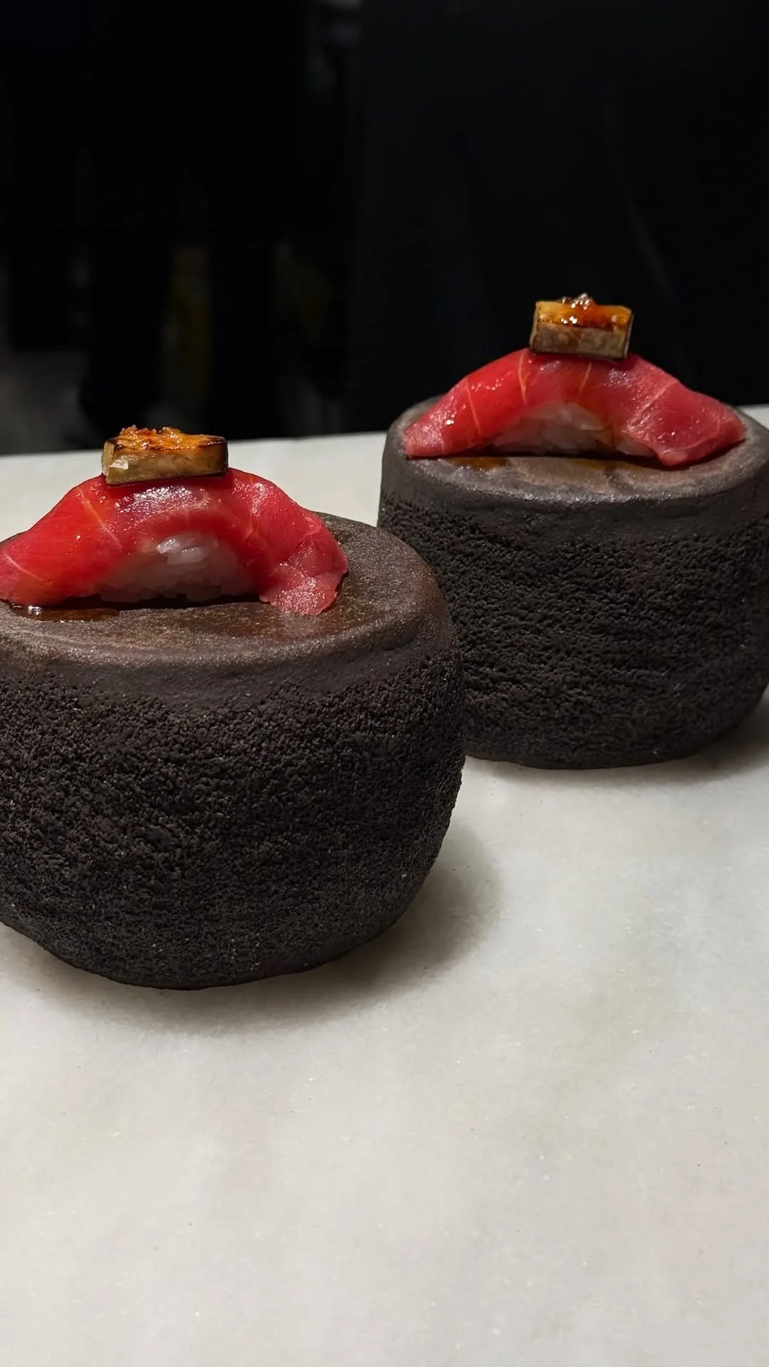 Two nigiri topped with red tuna and orange garnish on dark stone stands