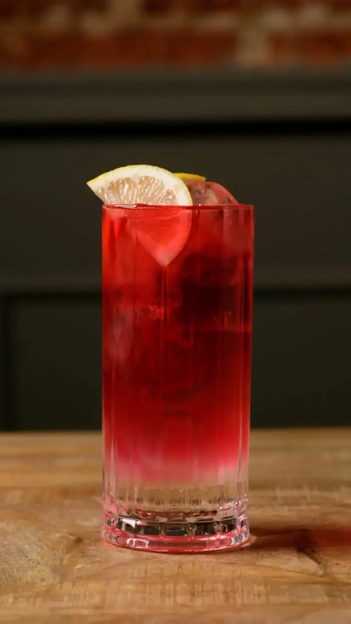 Tall red cocktail garnished with a lemon wheel on a wooden table