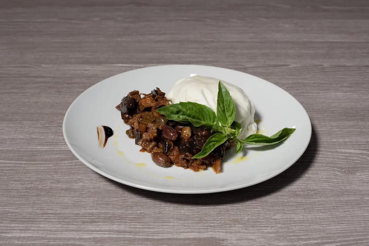 Burrata plated with a caponata-style eggplant and olive relish, basil garnish
