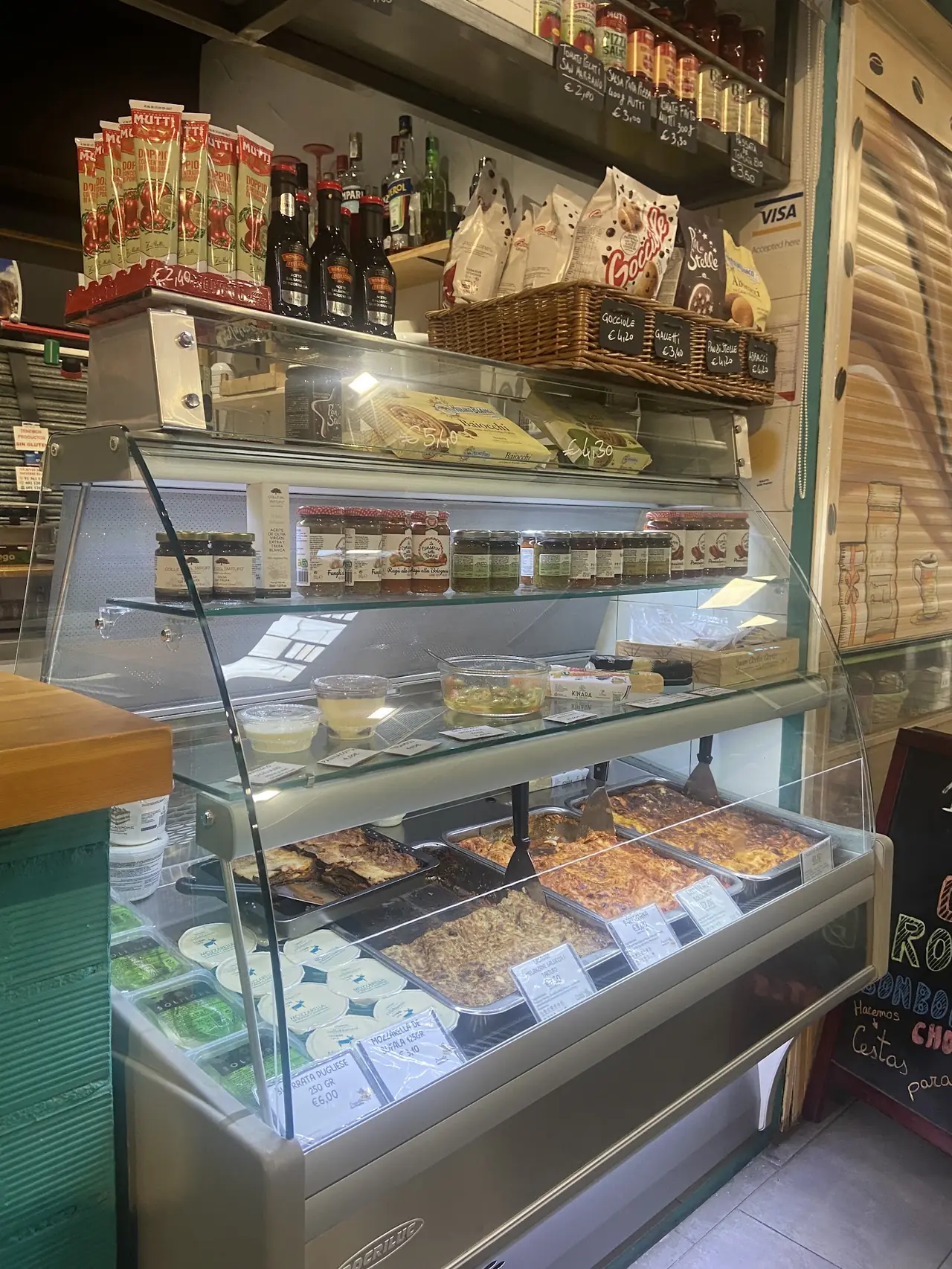 Deli display case with trays of prepared lasagna and fresh mozzarella for sale