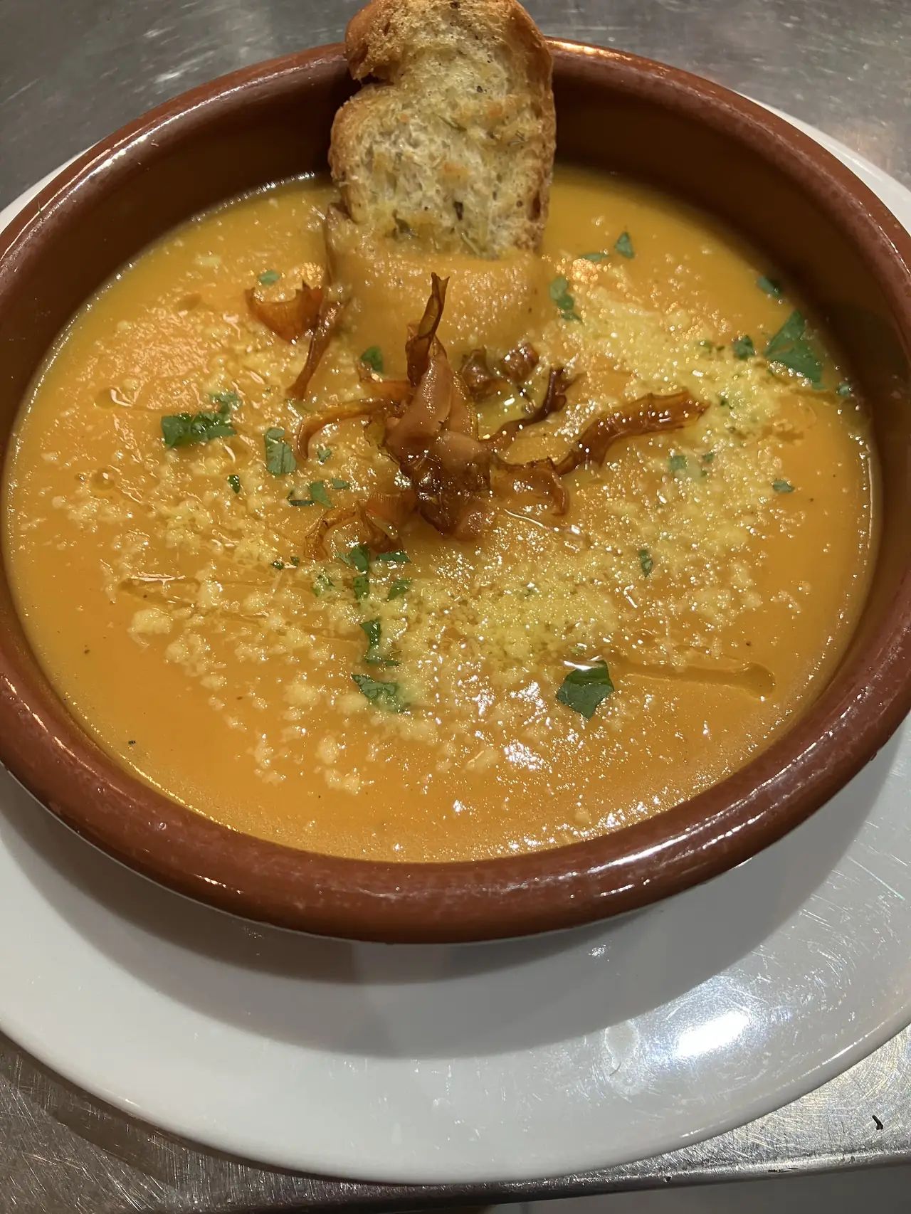 Bowl of pumpkin soup topped with crispy shallots, parsley and a bread crostino