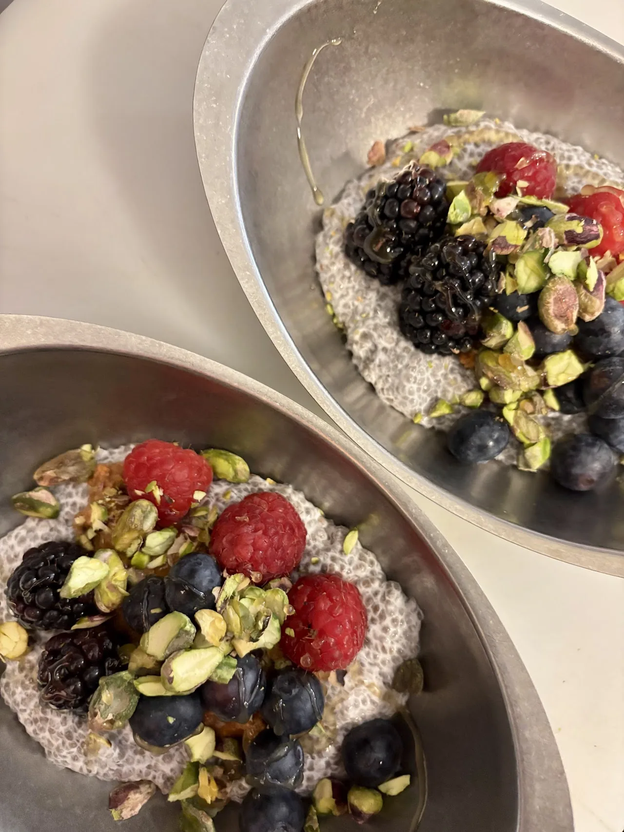 Two bowls of granola topped with berries and pistachio