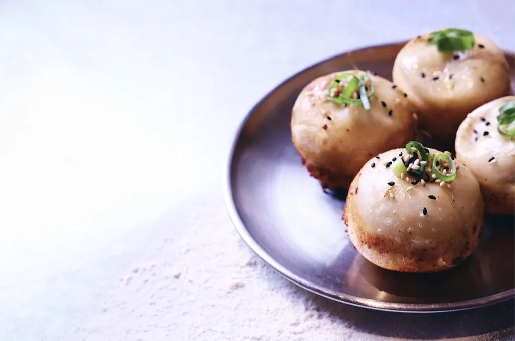 Pan-fried buns sprinkled with sesame seeds and spring onion on a metal plate