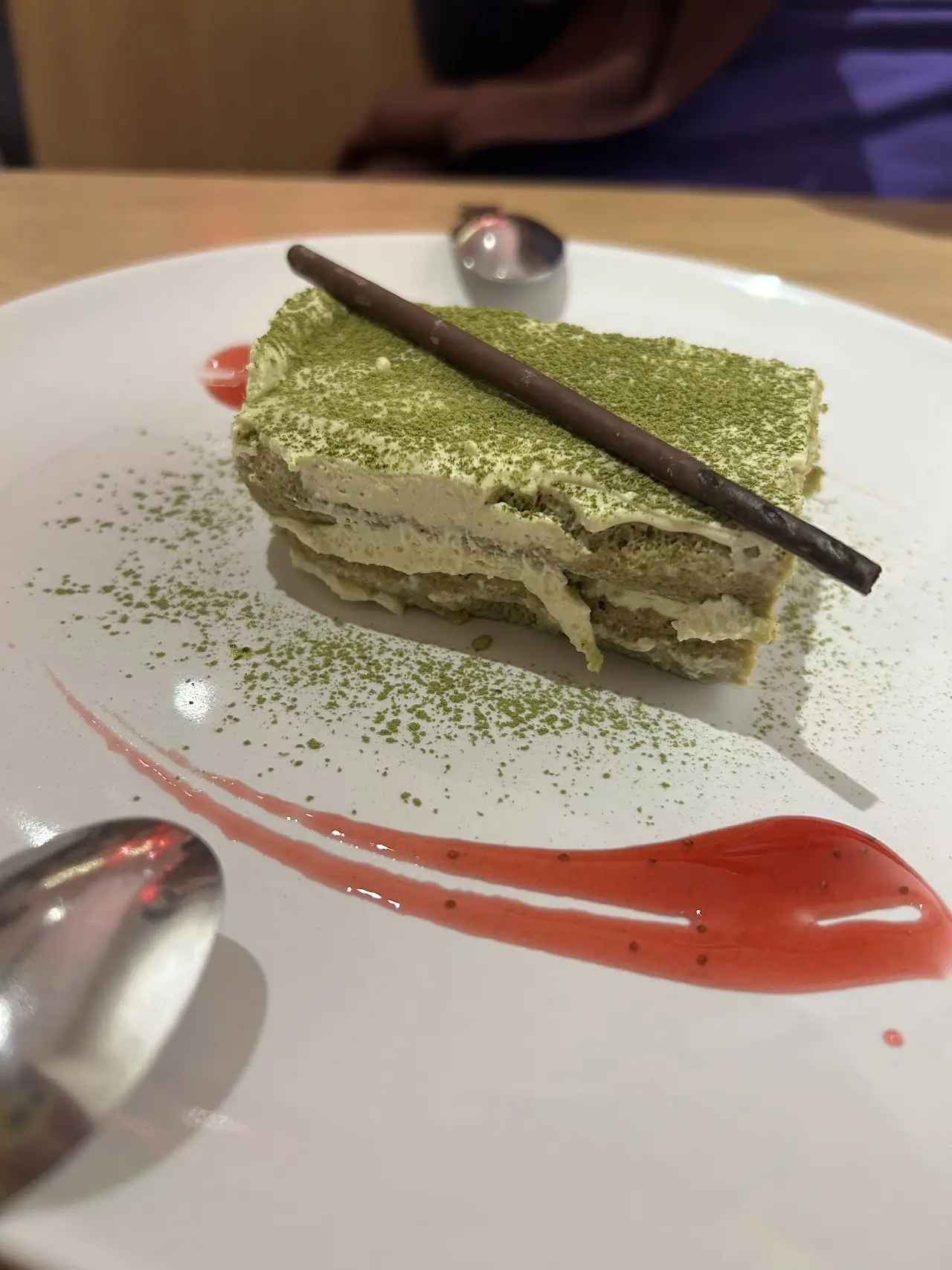 A slice of matcha layer cake with a red fruit sauce swirl on the plate.