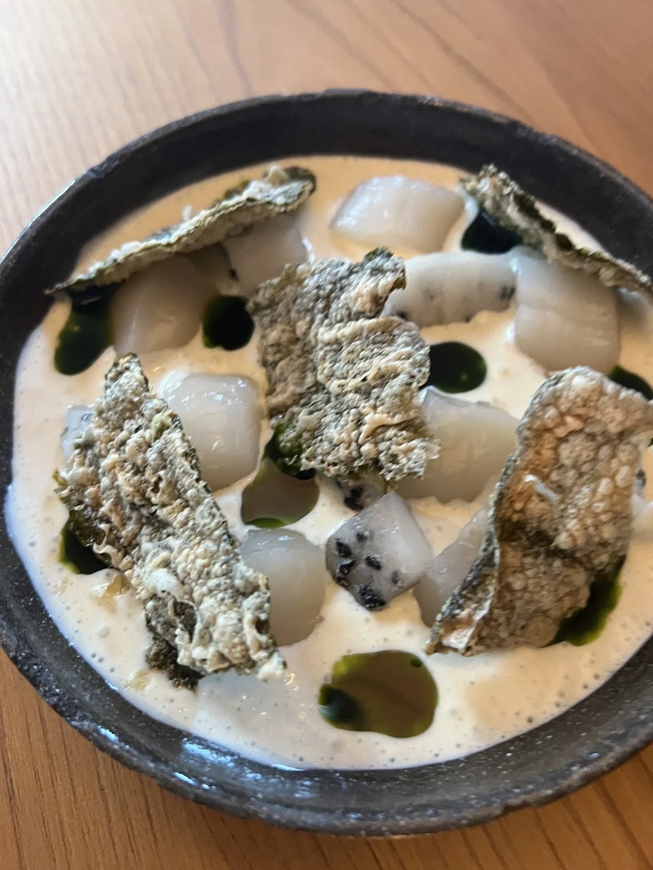 Slices of white seafood with dark crisps in a creamy white sauce in a dark bowl