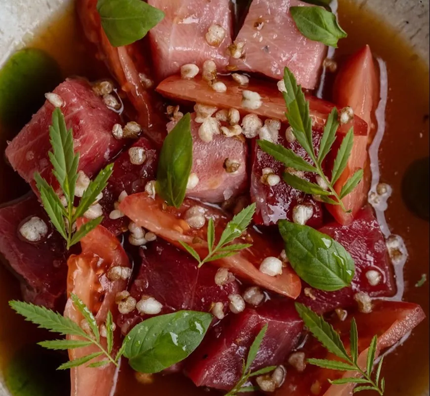 Cubes of raw tuna with tomato, fresh herbs and small seeds in a red sauce