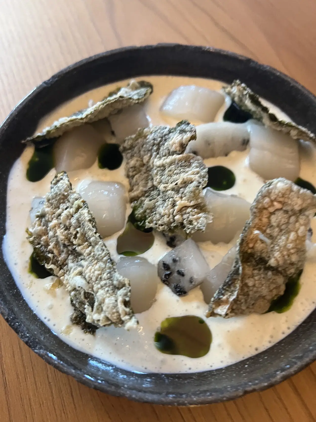 Seared scallops and mushroom in a creamy sauce with herb oil, in a dark bowl.