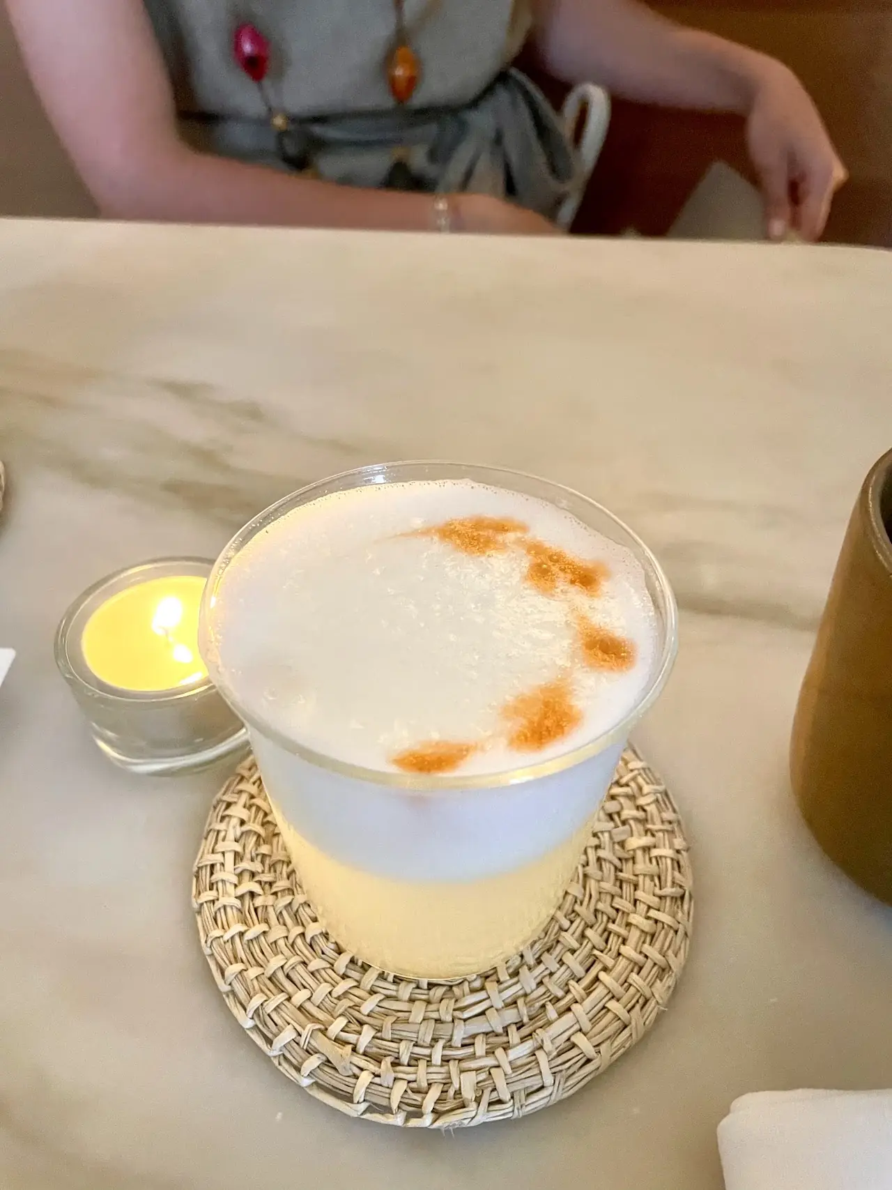 A frothy cocktail dusted with an orange-red spice on top, served in a glass on a woven coaster.
