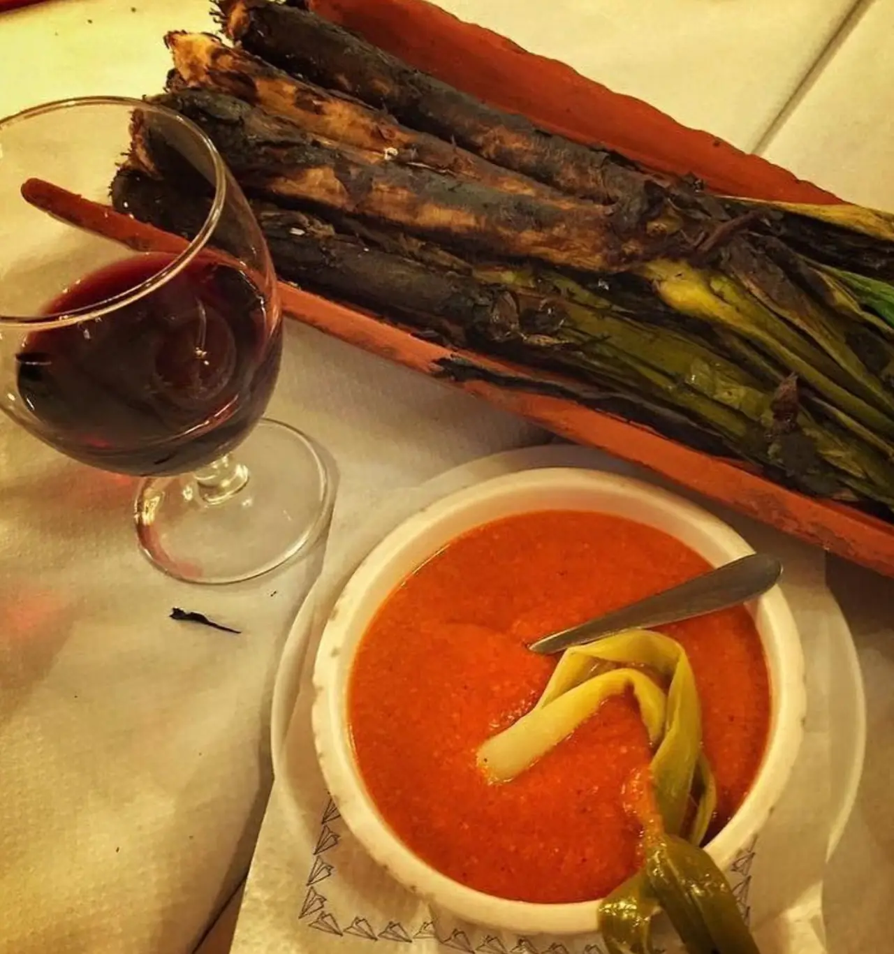 Charred grilled asparagus alongside a bowl of red romesco-style sauce, with a glass of red wine, at Restaurant La Llar de Foc