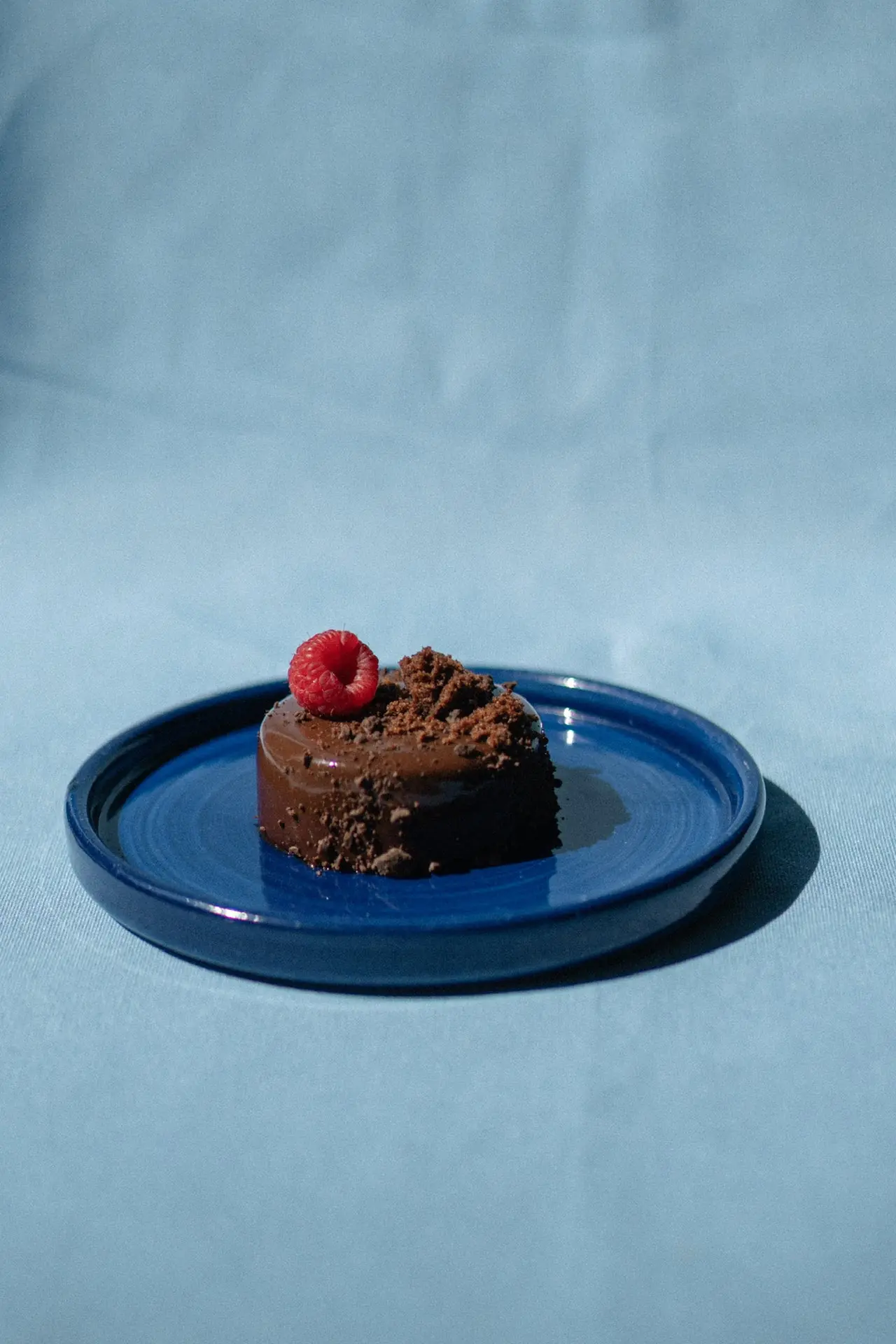A slice of chocolate cake with a raspberry on a blue plate