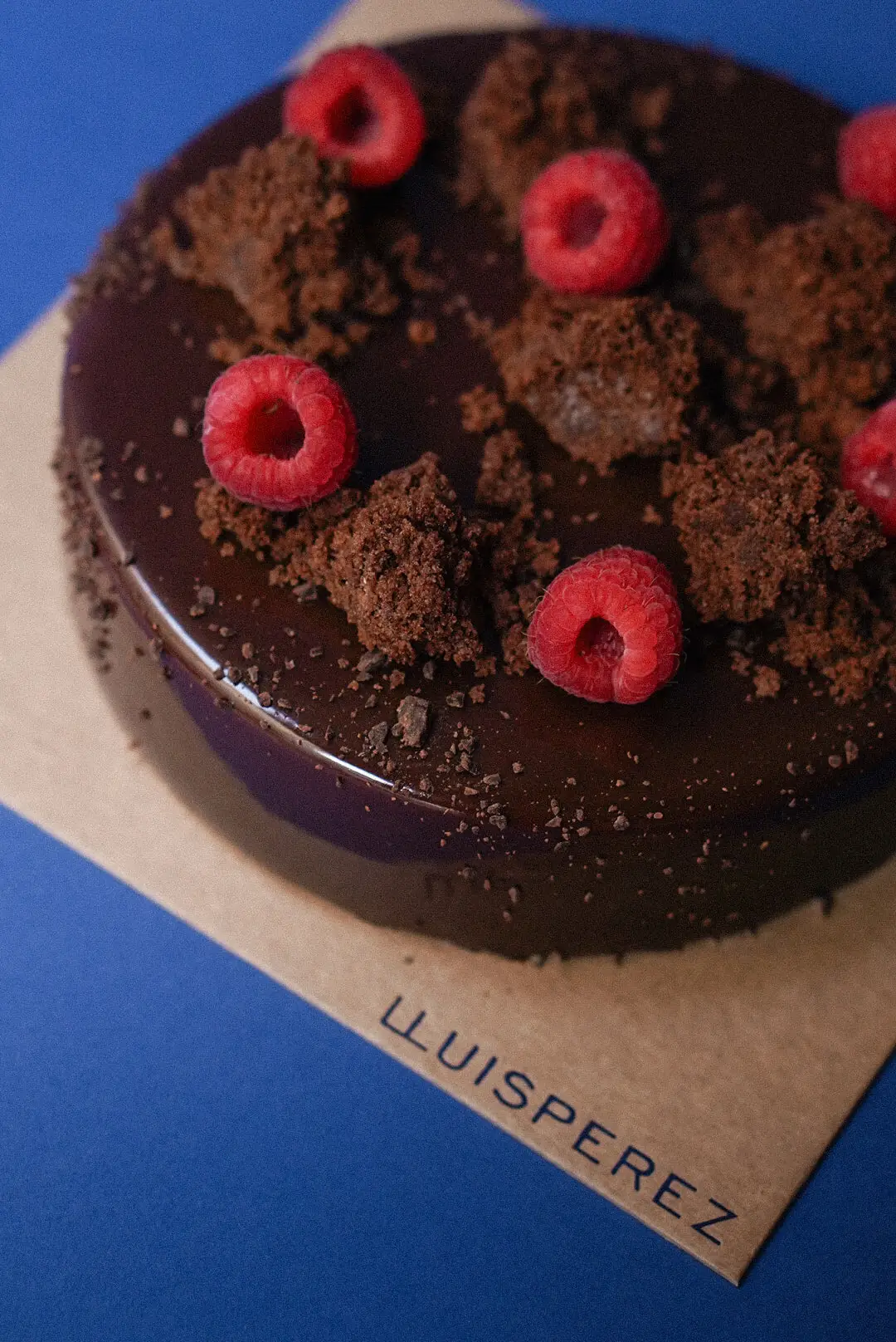 A whole chocolate cake topped with fresh raspberries and cocoa crumb at Lluís Pérez Pastisser
