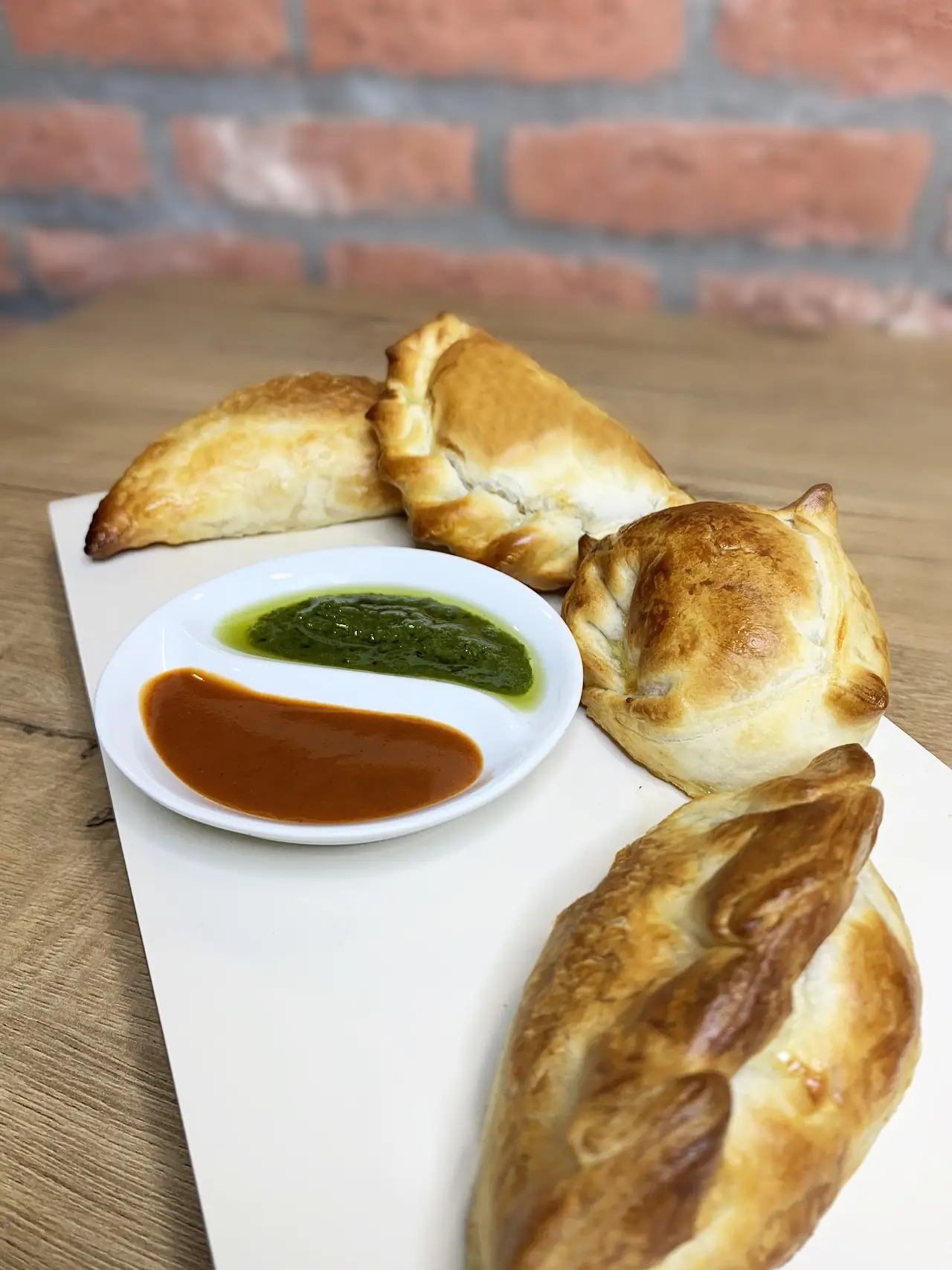 Three golden empanadas served with green and red dipping sauces