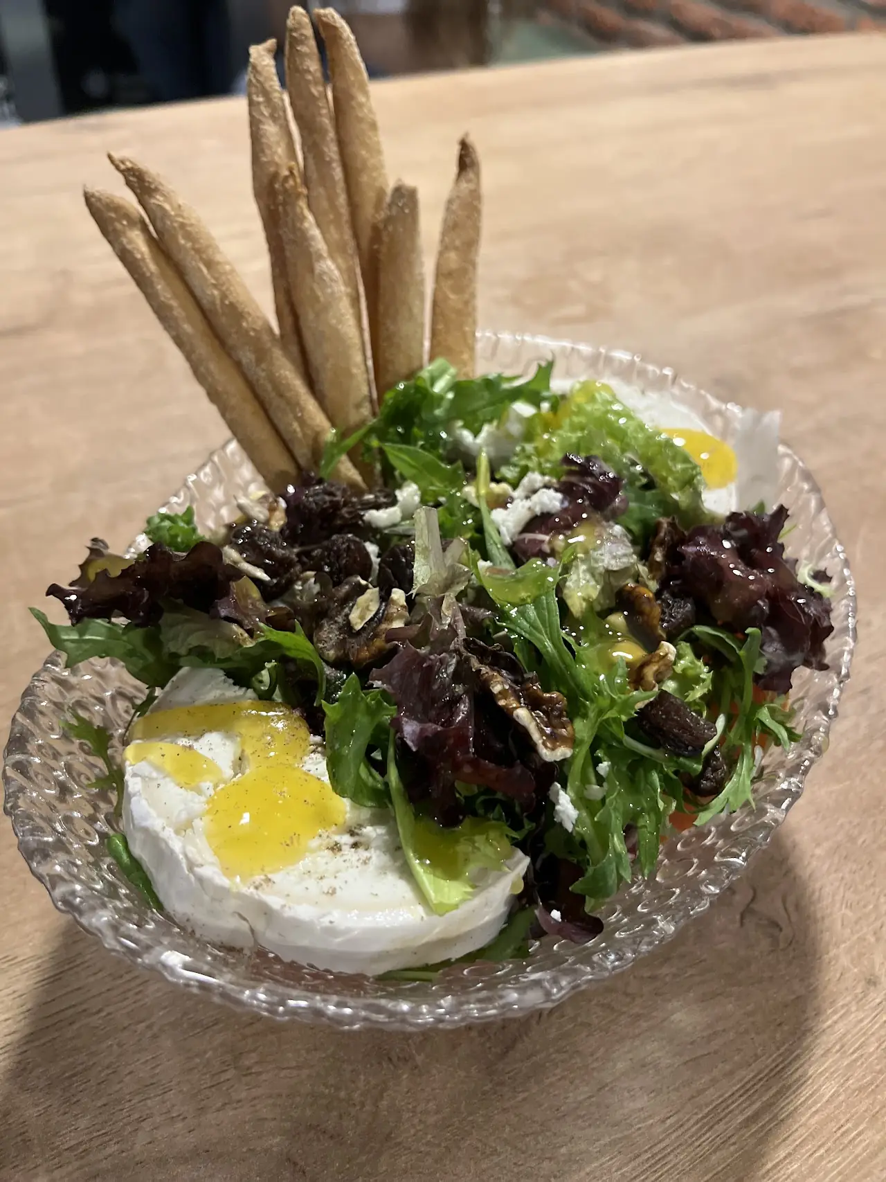 A salad of mixed greens with soft white cheese and an egg, served with breadsticks