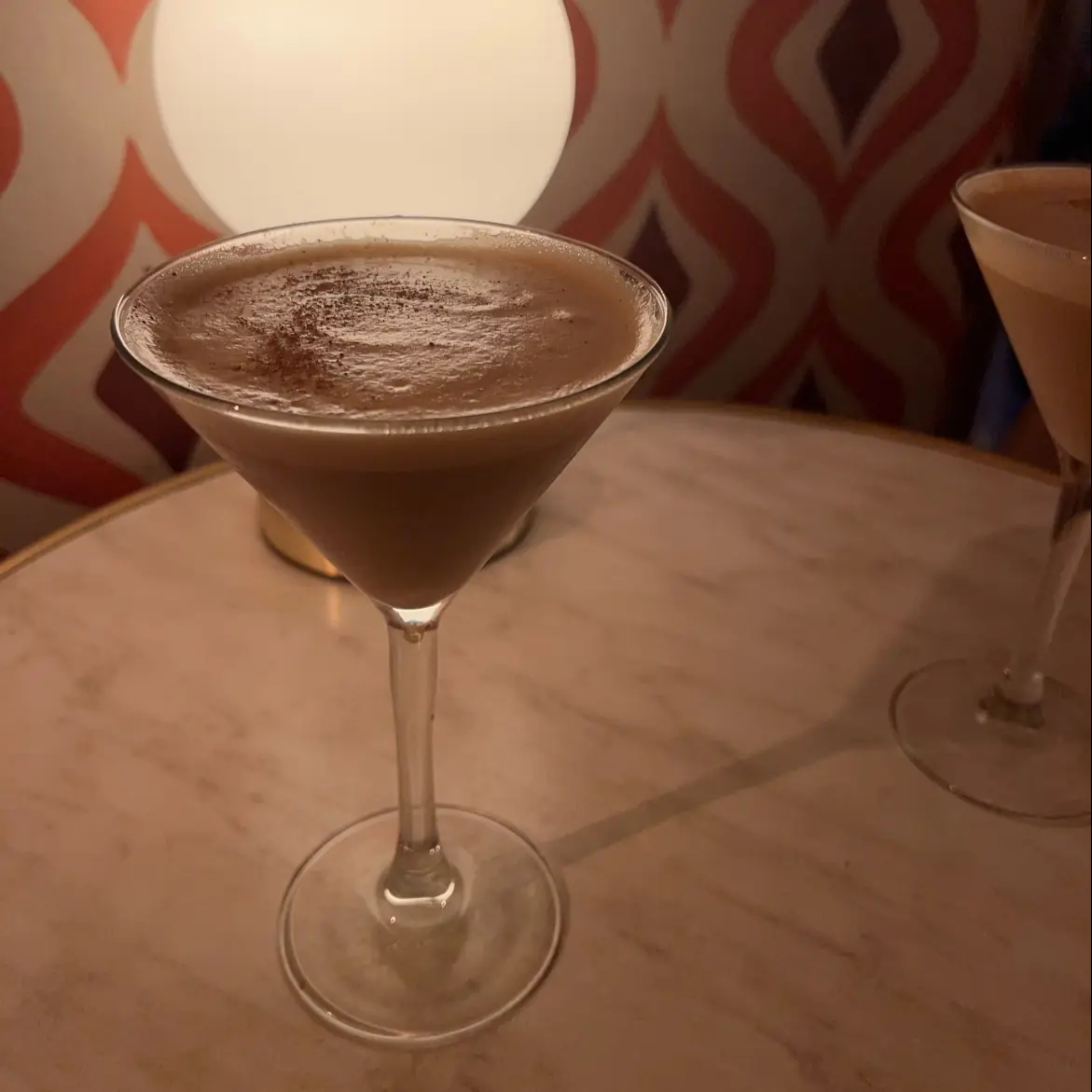 A chocolate-coloured cocktail in a coupe glass with a cocoa-dusted top