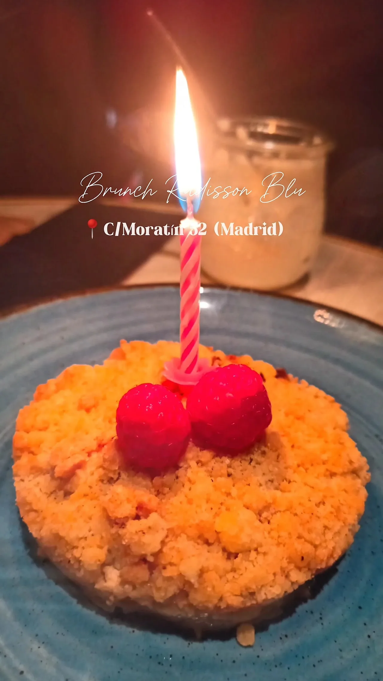 A carrot cake dessert with a lit candle and cherries on top