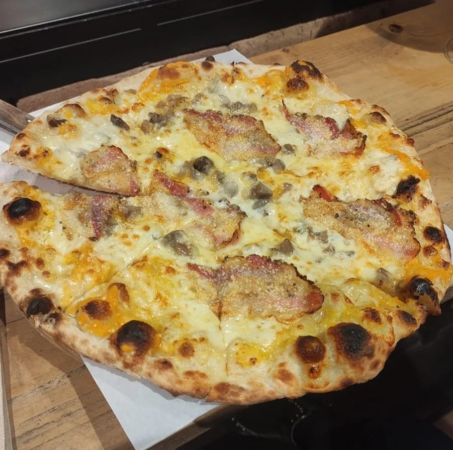 A whole pizza with melted cheese and pieces of ham on a paper-lined tray