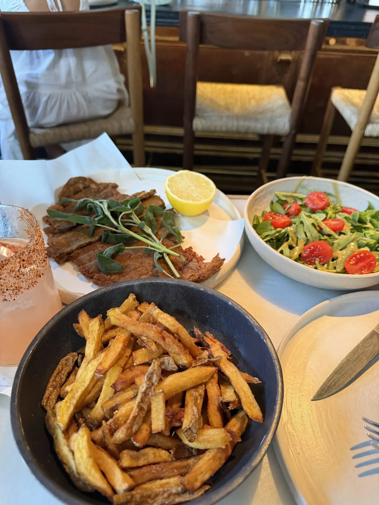 Table spread of fries, breaded meat with sage and lemon, tomato salad and a cocktail