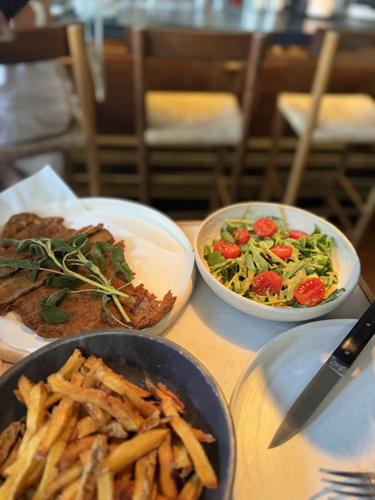 Fries, breaded meat with sage, and a tomato arugula salad on a table