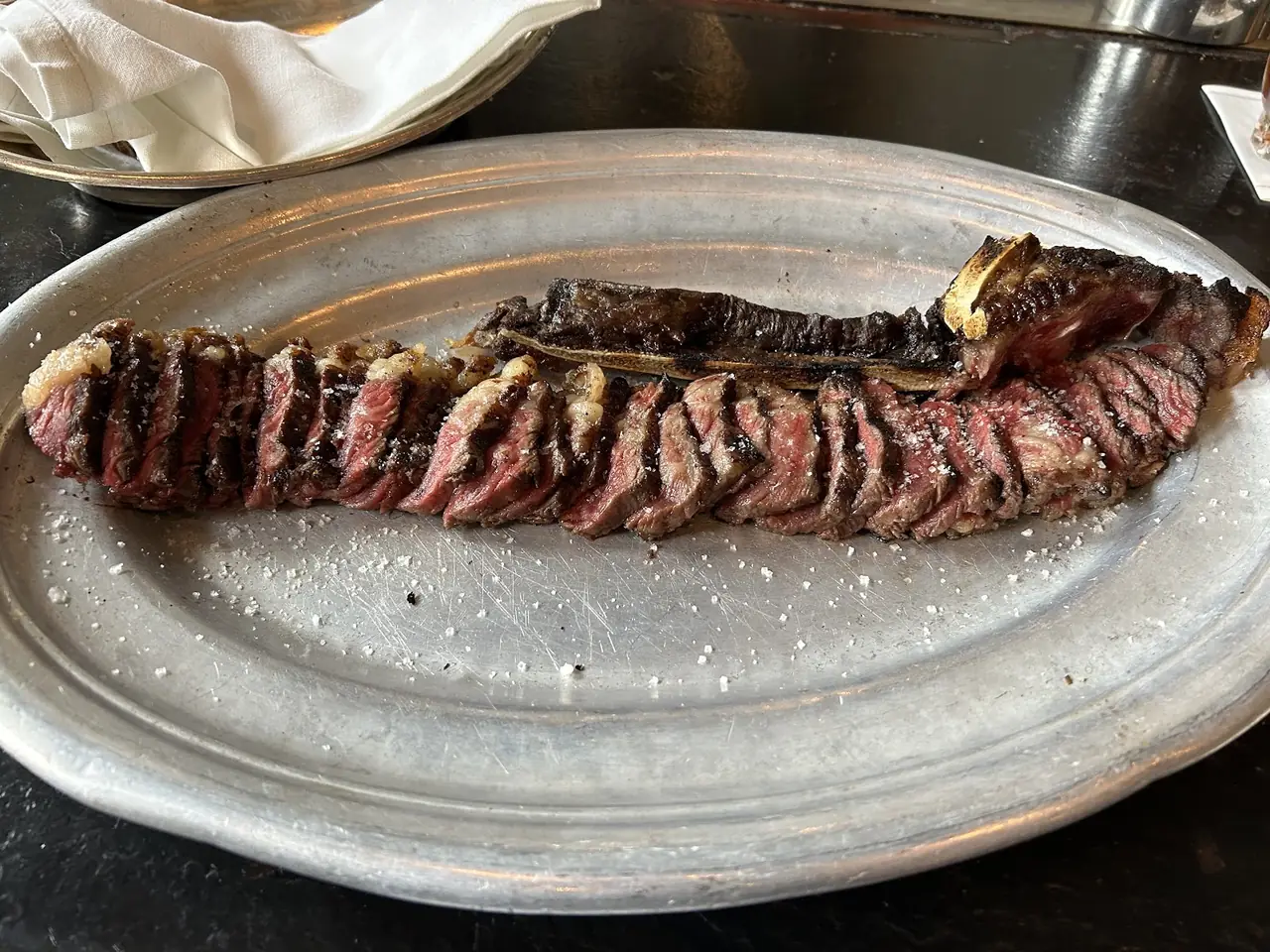 Sliced grilled steak on the bone, salted, plated on a metal tray
