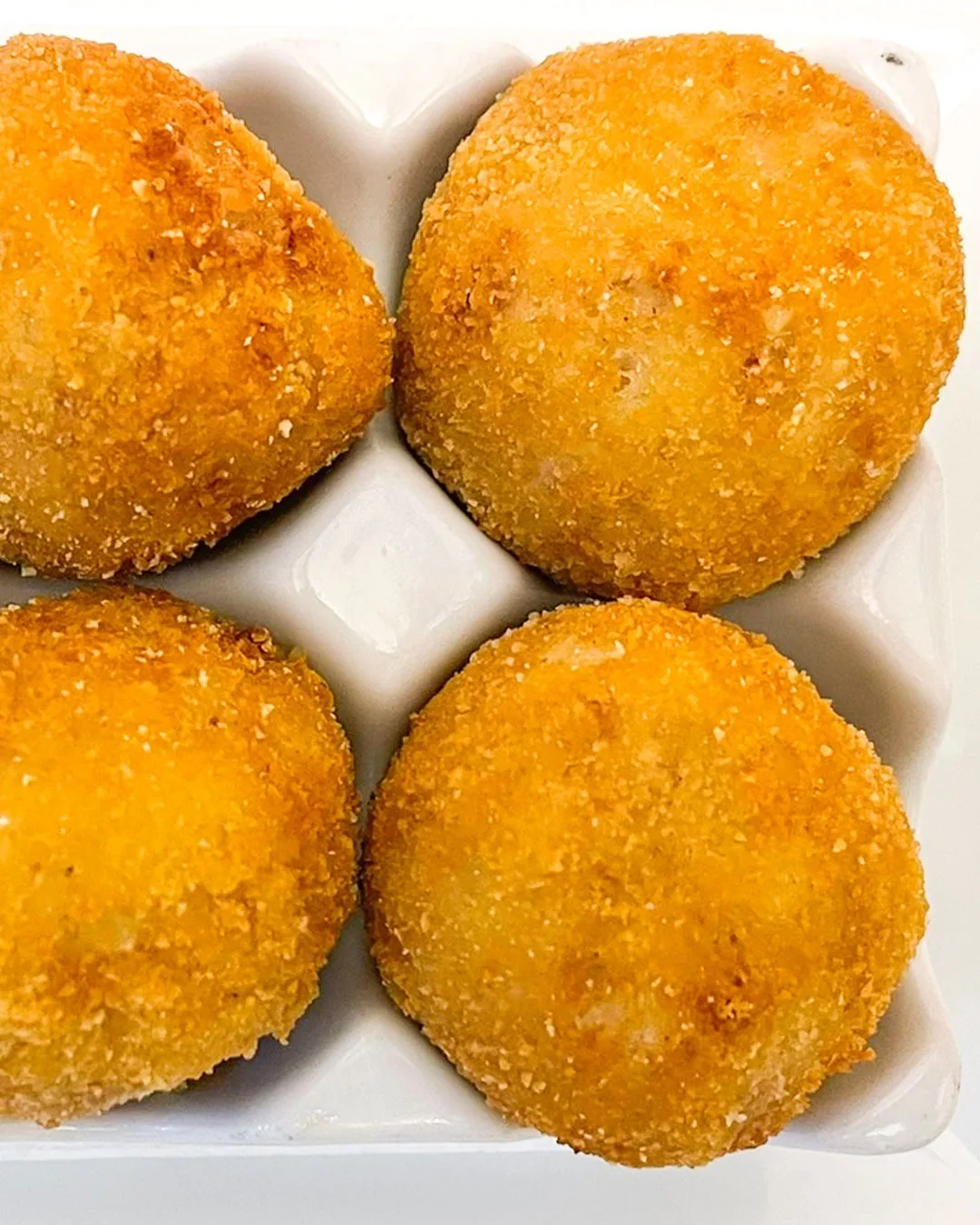 Four golden breaded croquettes in a white dish
