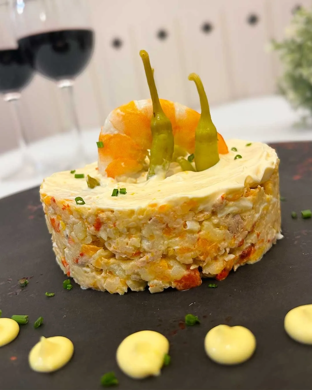 A round stack of potato salad topped with an egg and green peppers on a dark plate