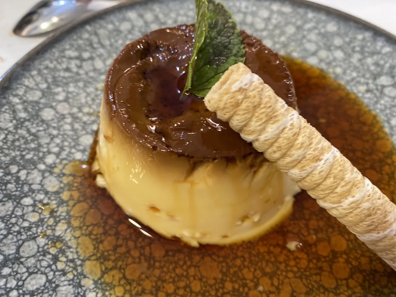 A flan dessert with caramel sauce and a rolled wafer
